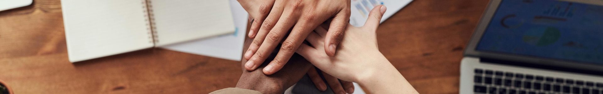Diverse professionals unite for teamwork around a wooden table with laptops and documents.